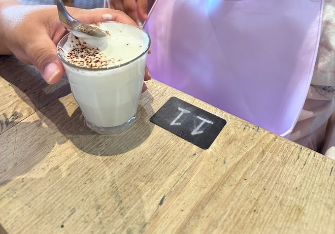 A glass latte with cocoa-dusted foam on a wooden table